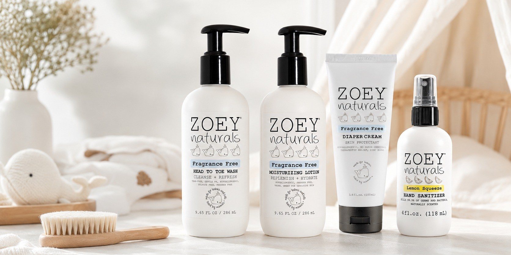 Zoey Naturals wash, lotion, diaper cream and hand sanitizer lined up on a white shelf with a wooden baby brush and dried flowers