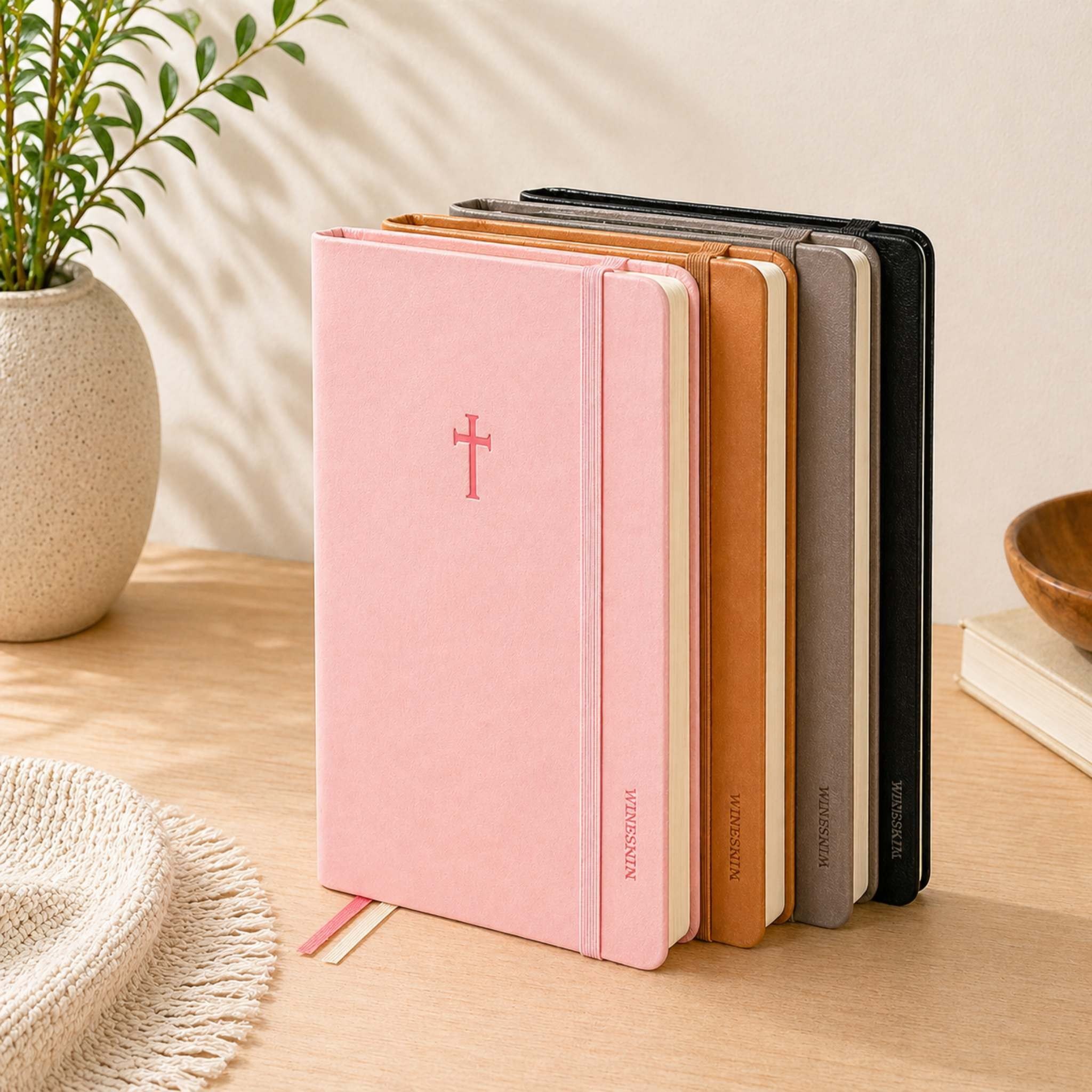 Swanson Christian Products journals in pink and leather tones on a wooden table