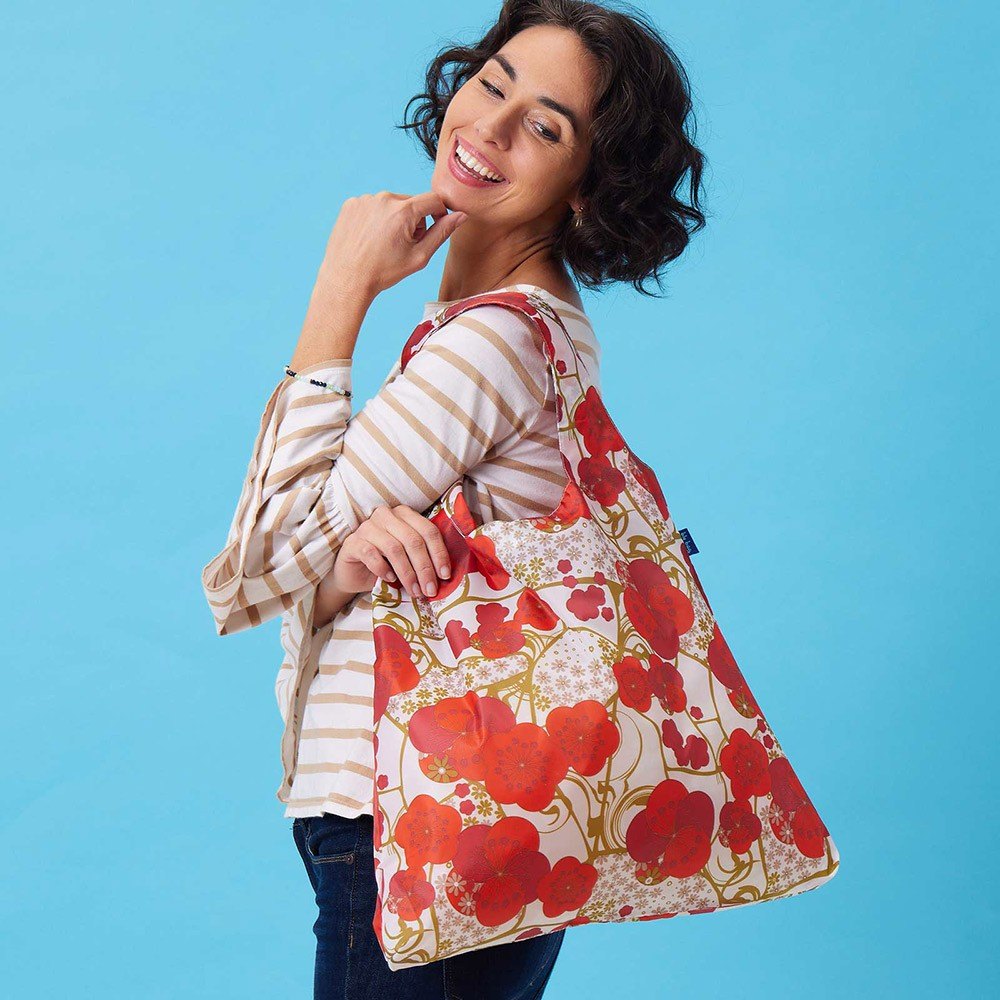 A smiling woman carrying a red floral Rockflowerpaper tote against a bright blue wall